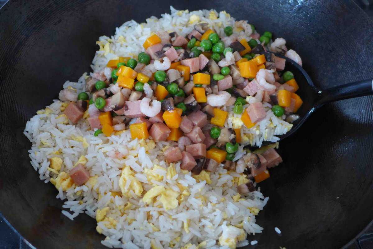 adding vegetables and meat to fried rice and eggs.