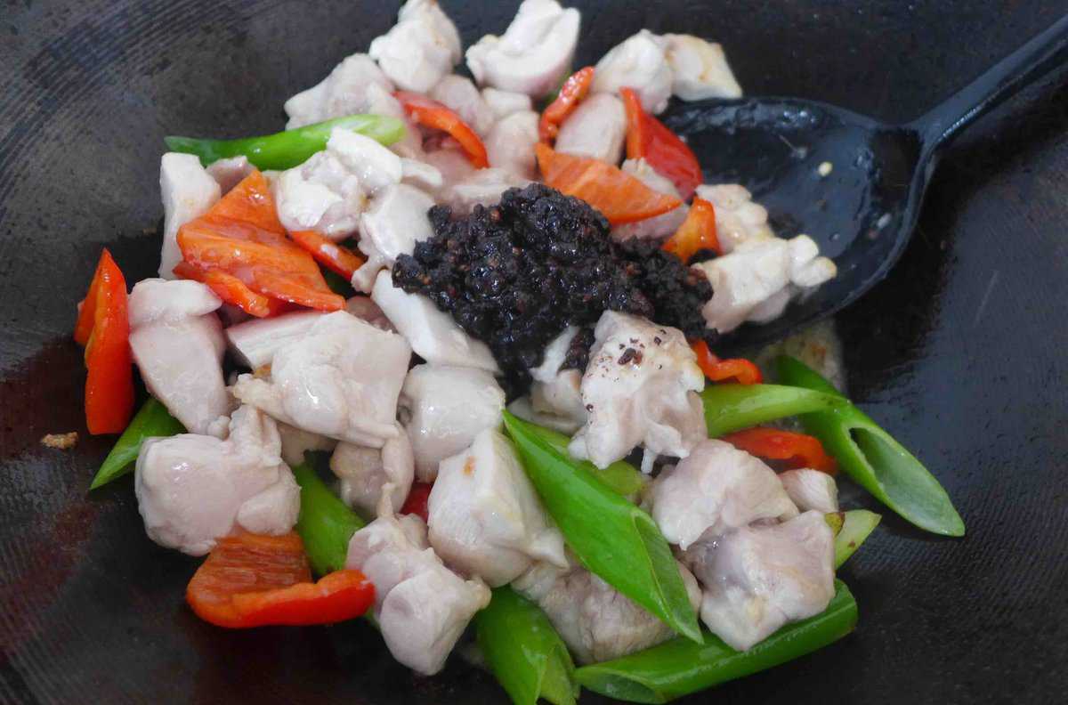 Adding black bean sauce to chicken and vegetables.