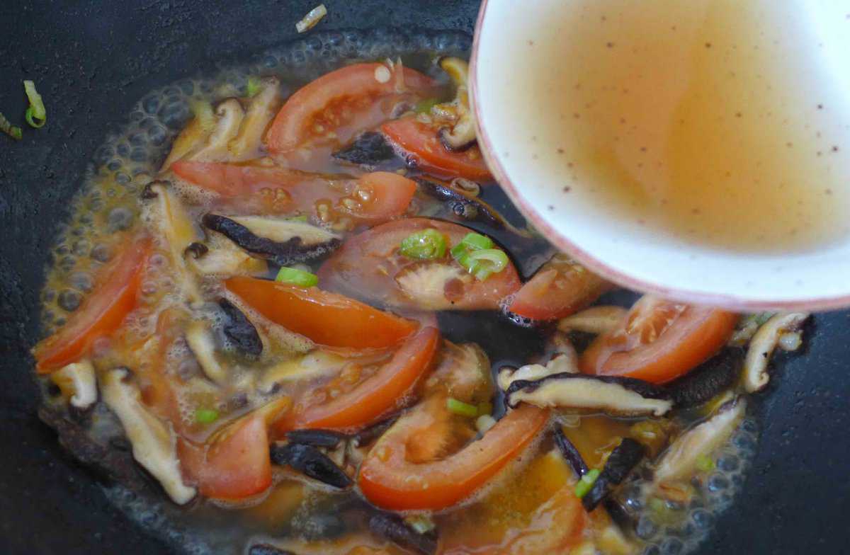 pouring mushroom water over tomato and mushrooms.