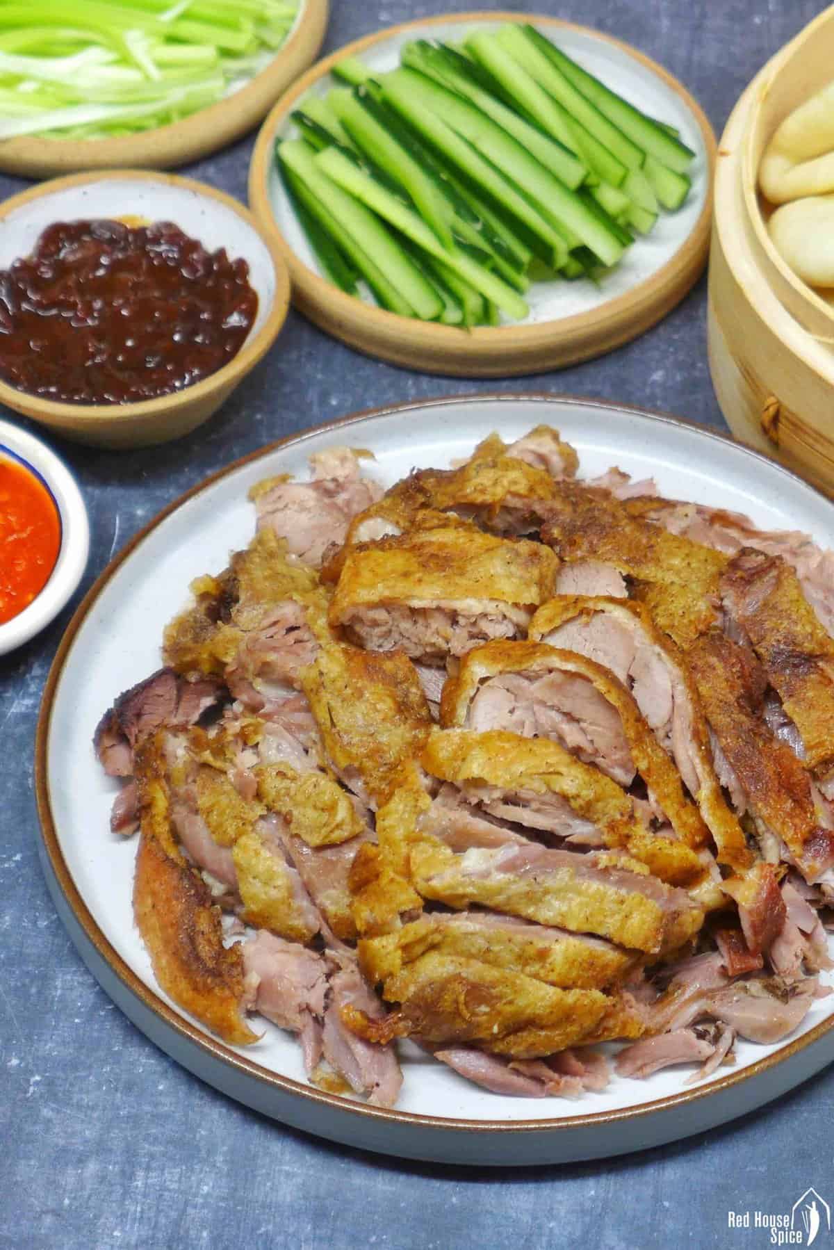 A plate of aromatic crispy duck with buns, vegetables and sauces on the side.