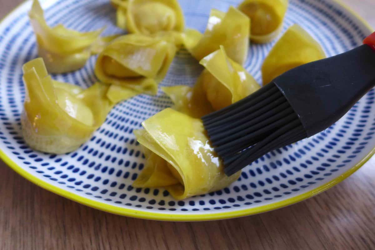 brushing oil over uncooked wontons.