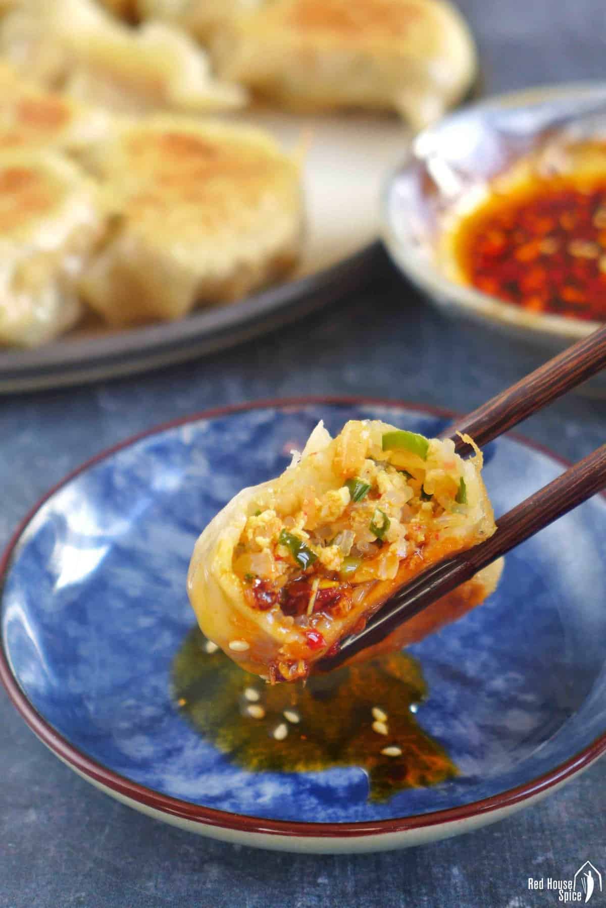 chopsticks holding a dumpling showing its kimchi filling.