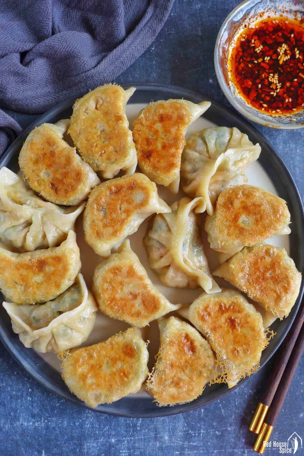 pan-fried kimchi dumplings on a plate with chili oil on the side.