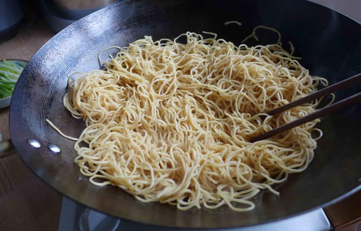 spreading cooked noodles in a wok.