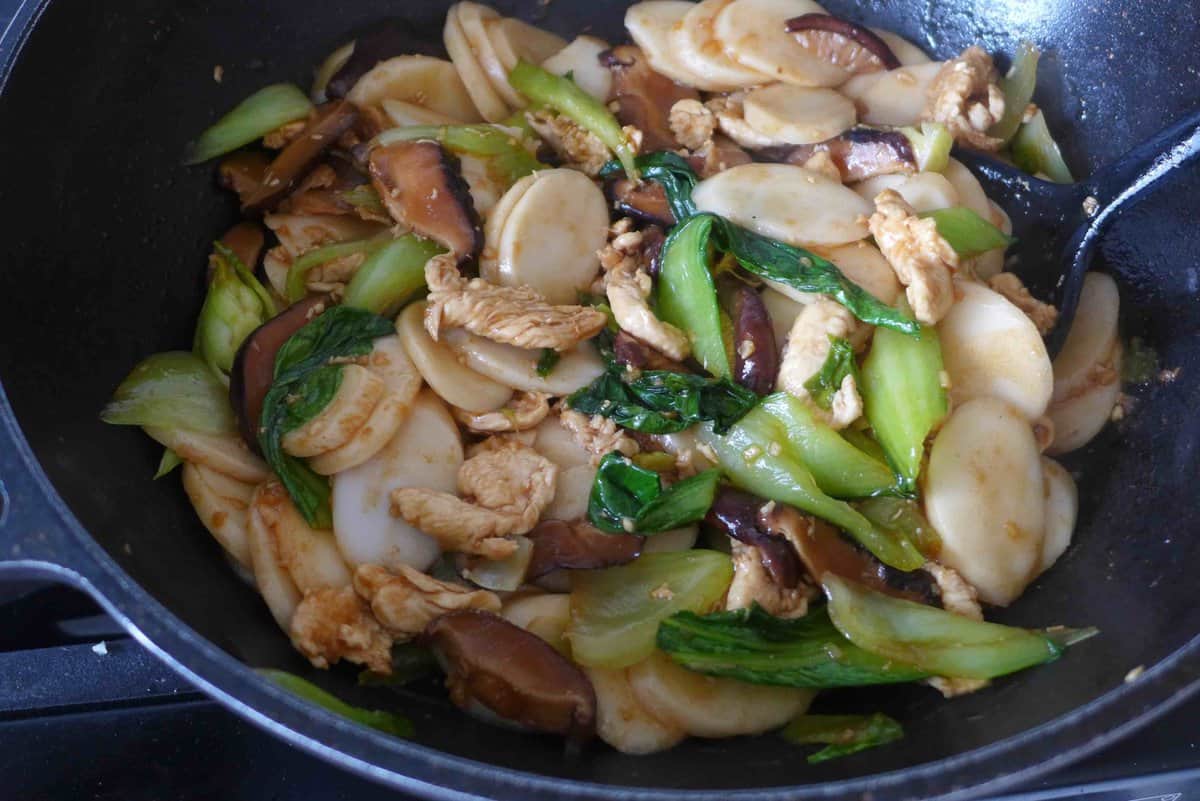 stir-frying rice cakes with chicken and vegetables in a wok.