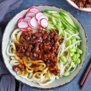 a bowl of Zha Jiang Mian, noodles with brown pork sauce and vegetable toppings.