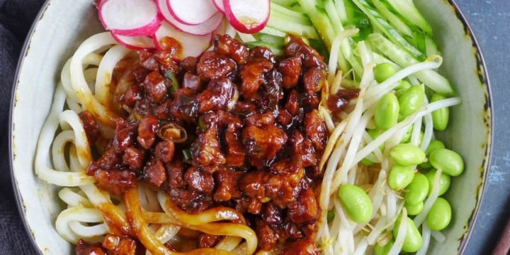 a bowl of Zha Jiang Mian, noodles with brown pork sauce and vegetable toppings.